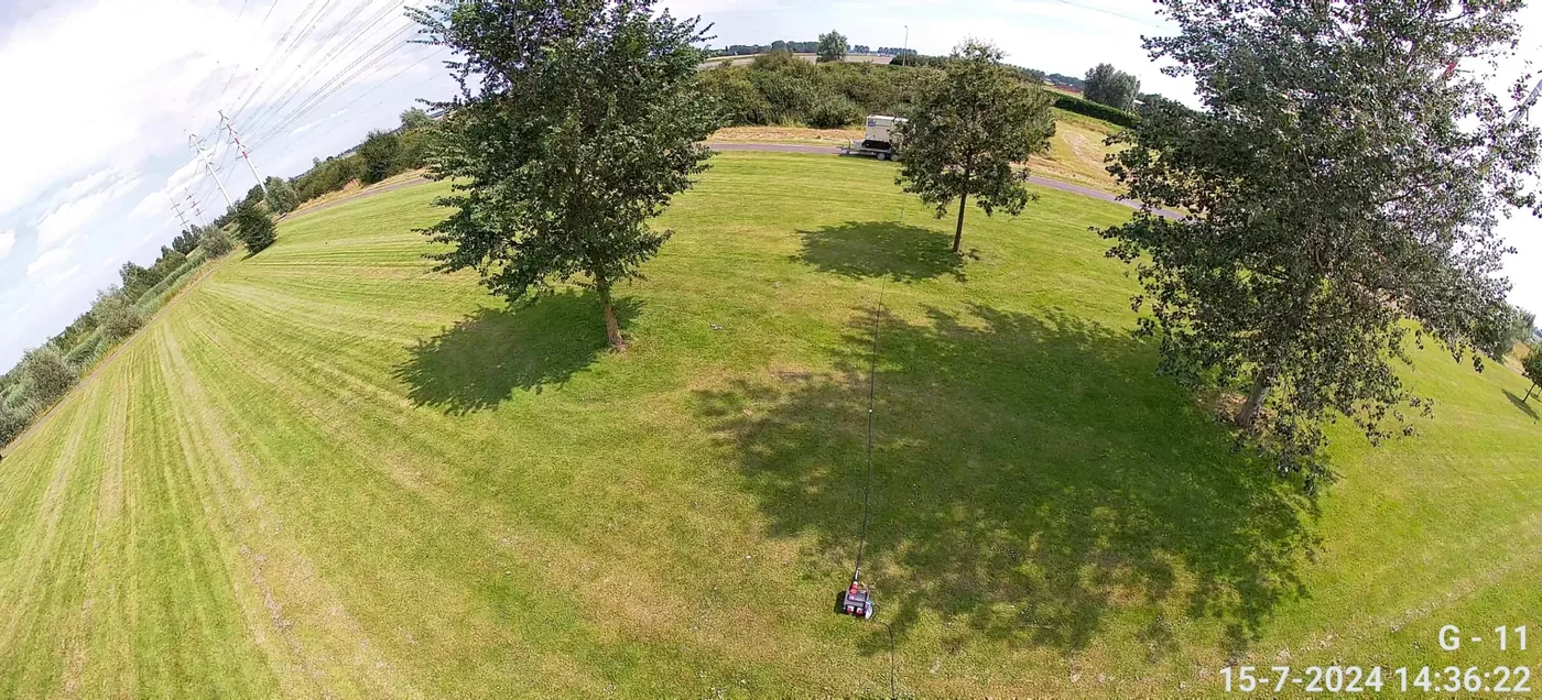 Camerabeeld van het grasveld en de bomenrij aan de rand van het terrein