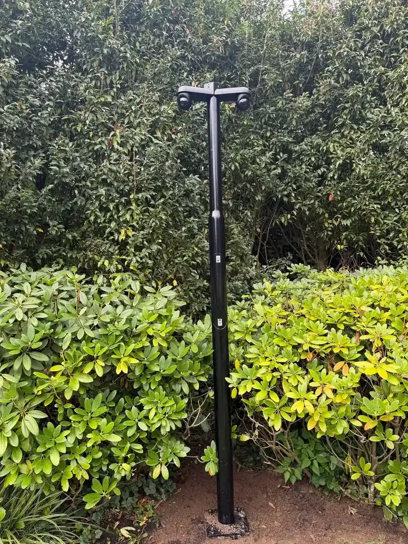 Dwarsarm met twee camera's boven op een zwarte paal in de beplanting