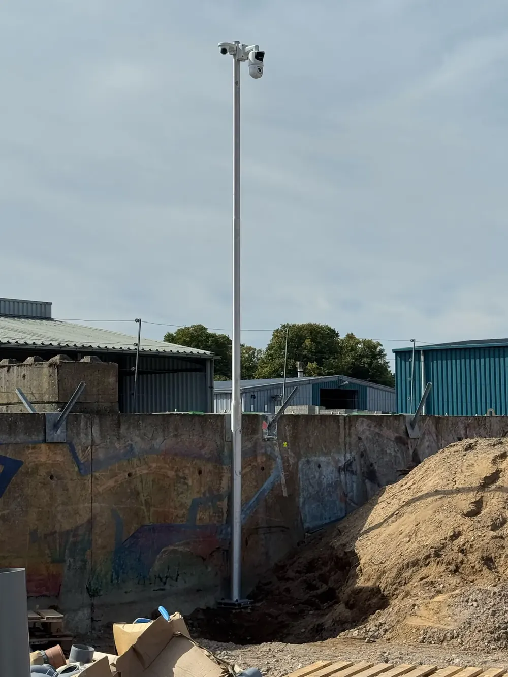 Hoge cameramast met draaibare camera en schijnwerper op een terrein in uitvoering